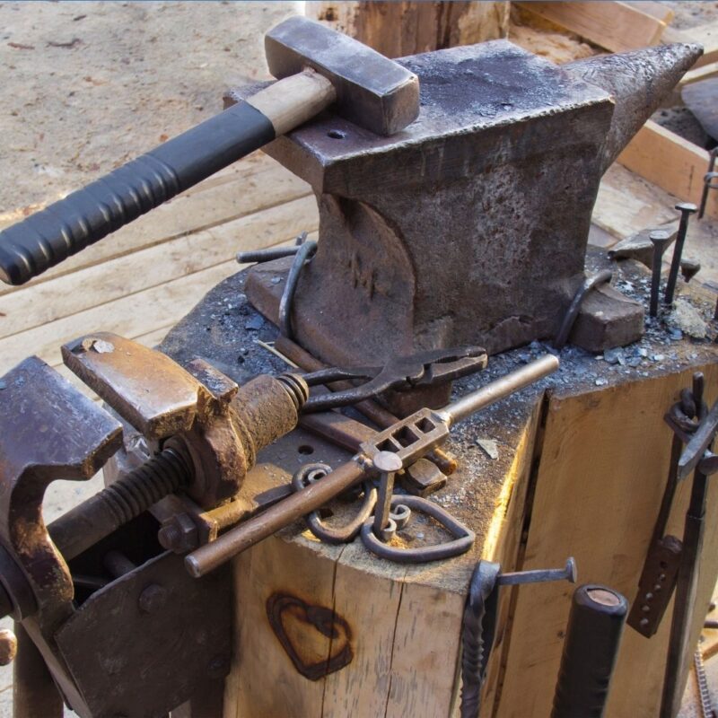 Blacksmith tools including an anvil, hammer, and vise on a wooden workbench