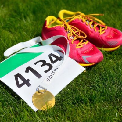 Running shoes beside a race bib and gold finisher medal on grass
