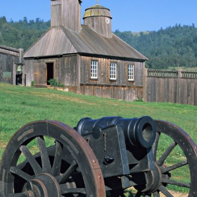 Historic wooden Russian fort building with cannon on grass in front