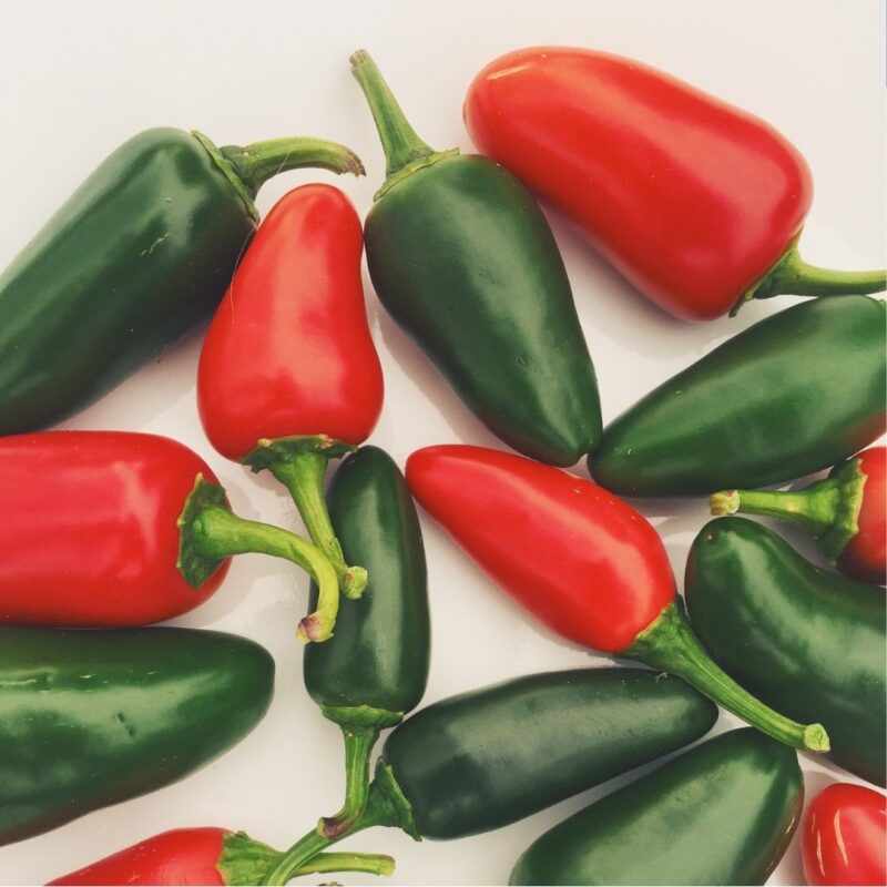 Red and green jalapeño peppers on a white surface