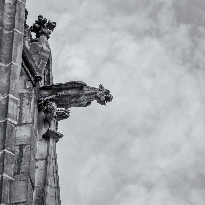 Stone gargoyle juts from a gothic building against a cloudy sky