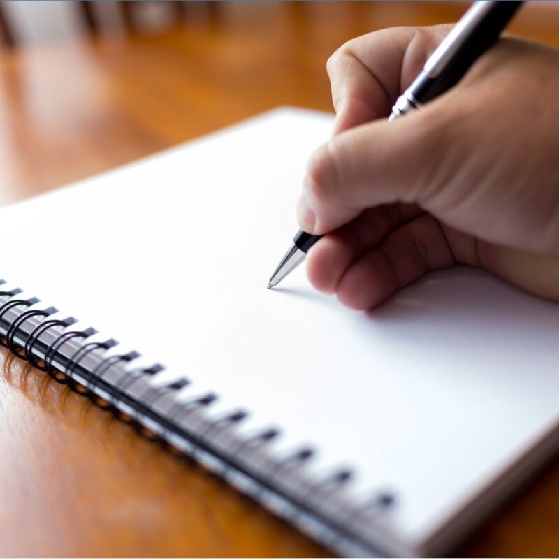 Hand holding a pen poised above a blank spiral notebook