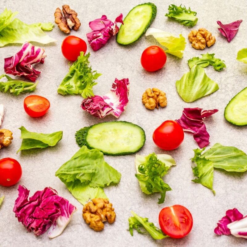 Assorted lettuce, cherry tomatoes, cucumber slices, red cabbage, and walnuts on a light surface
