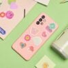 Various colorful stickers on a pink phone case and a green tumbler on a green surface