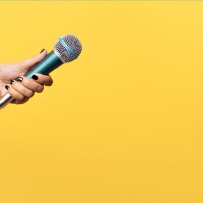 Hand holding a microphone against a yellow background
