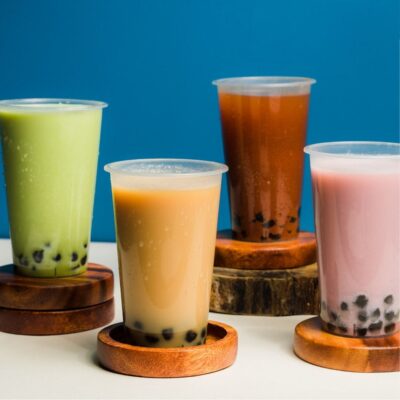 Four colorful bubble teas with tapioca pearls on wooden coasters