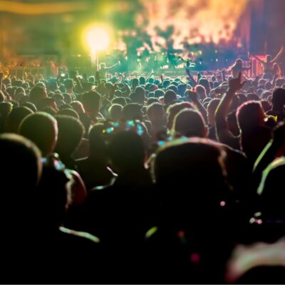 Large crowd of people enjoying a nighttime outdoor concert with colorful stage lights