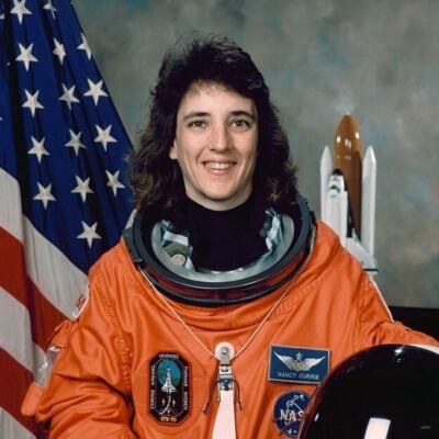 Astronaut Nancy Currie in NASA spacesuit with American flag and shuttle model