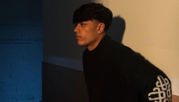 Danny Bretherton wearing a dark sweater standing against a wall