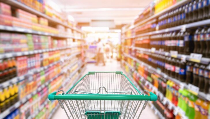 Empty shopping cart in a convenience store aisle with blurred shelves of products