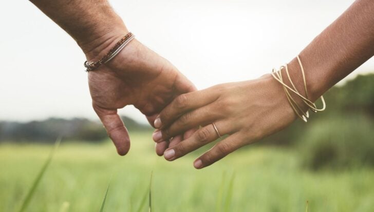 Two people holding hands in a grassy field, wearing bracelets