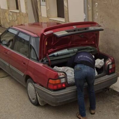 Person loading large wrapped bundles into the trunk of a red Rover sedan