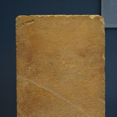 Weathered stone tablet with engraved ancient inscriptions along the top