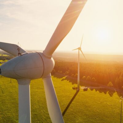 Wind turbines stand in a sunlit green field at sunset