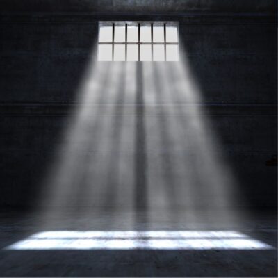 Dark prison cell with a barred window, sunbeams streaming onto the floor