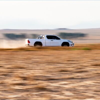 White Toyota Hilux pickup speeds across a dry desert plain