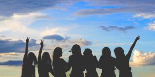 Silhouettes of several women standing together against a colorful sky, some raising their hands in celebration