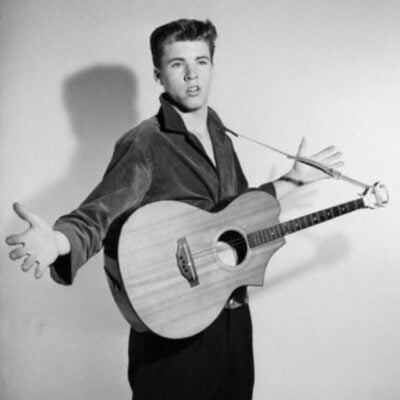 Ricky Nelson with acoustic guitar, arms outstretched