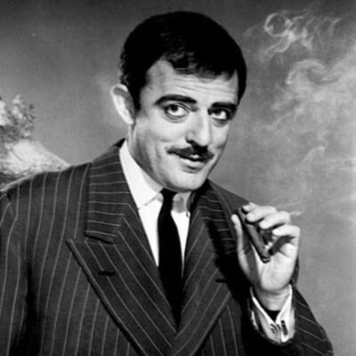 John Astin as Gomez in a pinstripe suit, holding a cigar