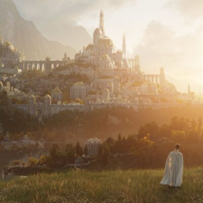 A person in a white cloak walks toward a vast, sunlit city with domes and arches on a hillside