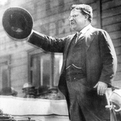 Theodore Roosevelt speaks after being shot, raising his hat