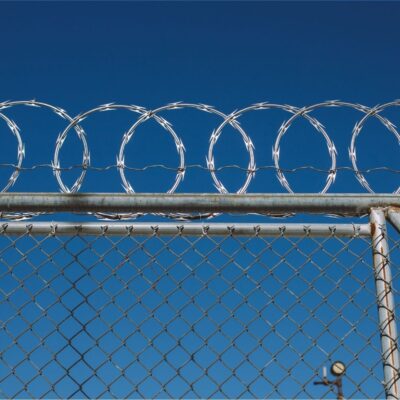 Razor wire loops above a chain-link fence against a blue sky