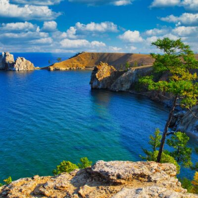 Blue Lake Baikal with a rocky shoreline, turquoise water, and pine trees on sunlit cliffs