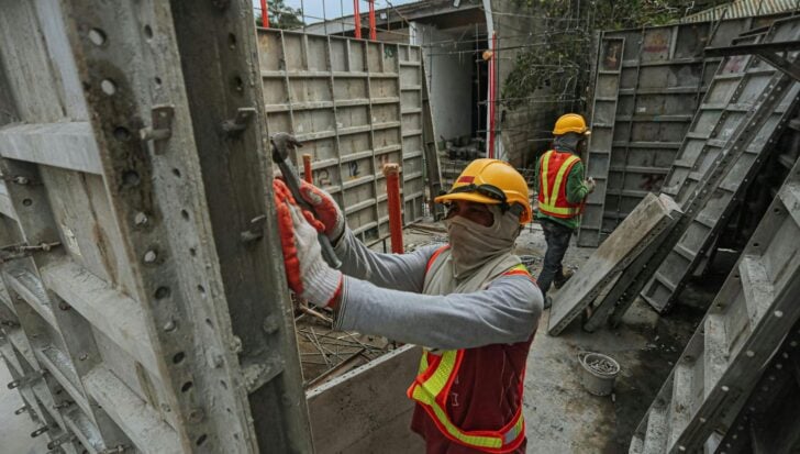 Construction workers wearing hard hats and safety vests work on assembling metal framework