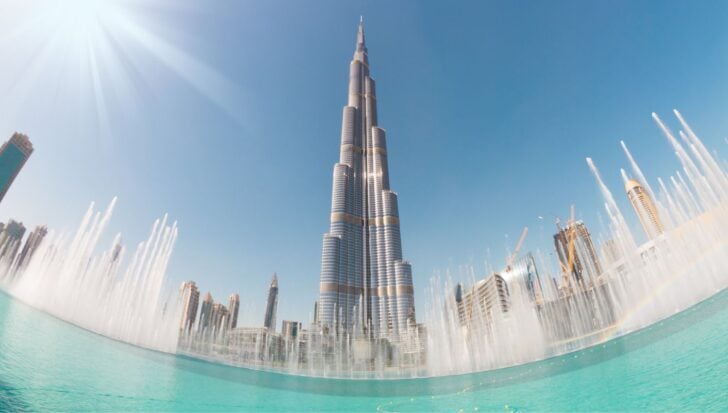 The Burj Khalifa surrounded by the Dubai Fountain, with skyscrapers and a clear blue sky in the background