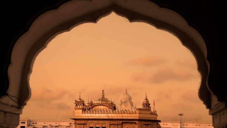 Golden Temple framed by ornate archway at sunset, highlighting Sikhism's heritage