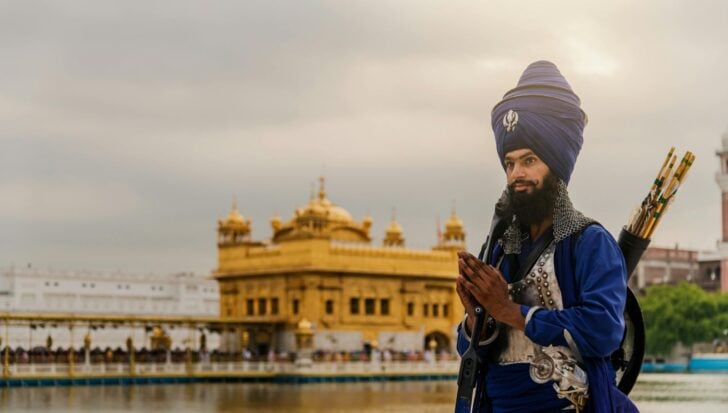 A Sikh man with traditional attire and uncut hair standing in front of the Golden Temple