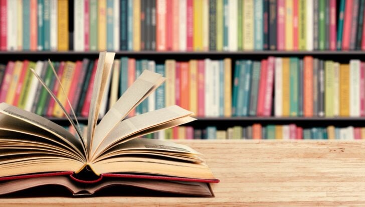 An open book on a wooden table with a colorful bookshelf in the background