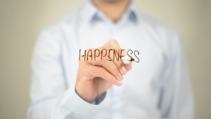 A person writing the word 'Happiness' on clear glass with a marker