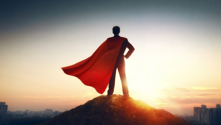 Person in a superhero costume with a cape standing on a hilltop at sunrise