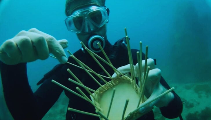 Person underwater wearing scuba gear, weaving a basket at the ocean floor