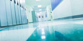 School hallway with blue lockers and reflective tiled floor, leading to closed doors