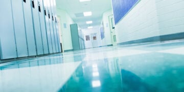 School hallway with blue lockers and reflective tiled floor, leading to closed doors