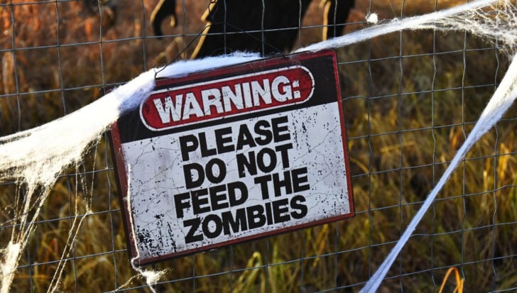 A warning sign on a wire fence saying: Please do not feed the zombies